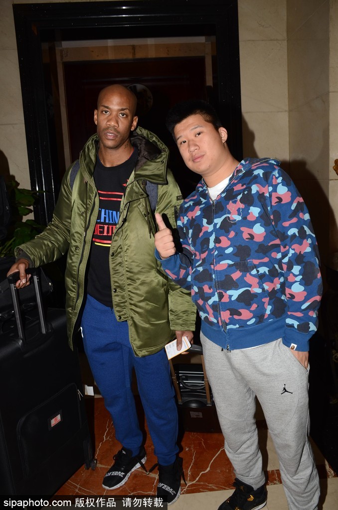 马布里身着休闲装，一手拖着行李箱，另一手亲切地搭在球迷肩上，脸上洋溢着标志性的笑容，仿佛与老朋友重逢般自然。