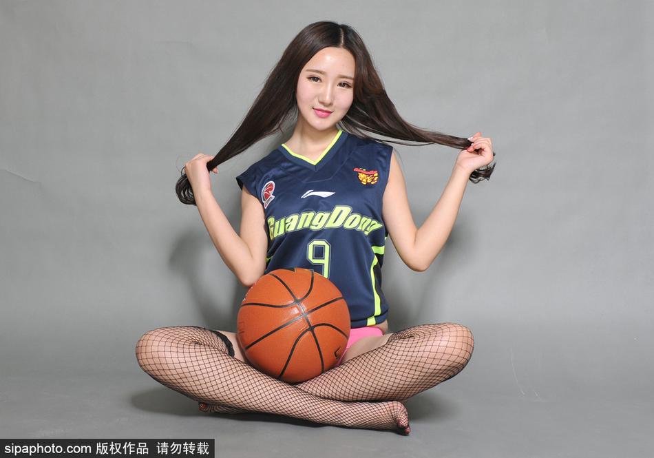 镜头聚焦在宝贝纤细的脚踝和脚下的篮球鞋上，黑色的丝袜在球场灯光下泛着微光，她身体微曲，双手指尖比出爱心，将赛场边的铁马变成了展示美丽的舞台。