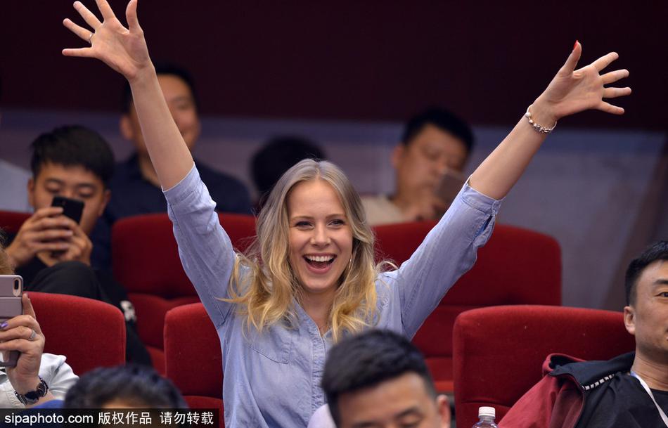 宝莲娜与身边的女伴一同望向球场，她展露灿烂笑容，似乎对比赛进程感到满意或为某个精彩瞬间喝彩，展现了欧洲球员家属特有的观赛文化。