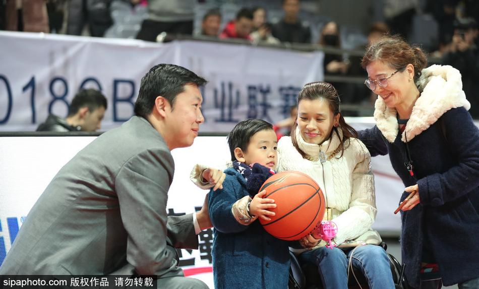 桑兰与丈夫黄健并肩坐在看台上，黄健神情专注地望向球场，桑兰则低头与怀中的儿子亲昵互动，一家三口其乐融融。