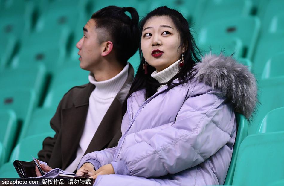 一位长发披肩的美女球迷身着宽松的黑色卫衣，双手轻轻托着下巴，目光越过球场护栏，温柔地投向赛场，眼神中满是对主队下一次精彩进攻的期待。