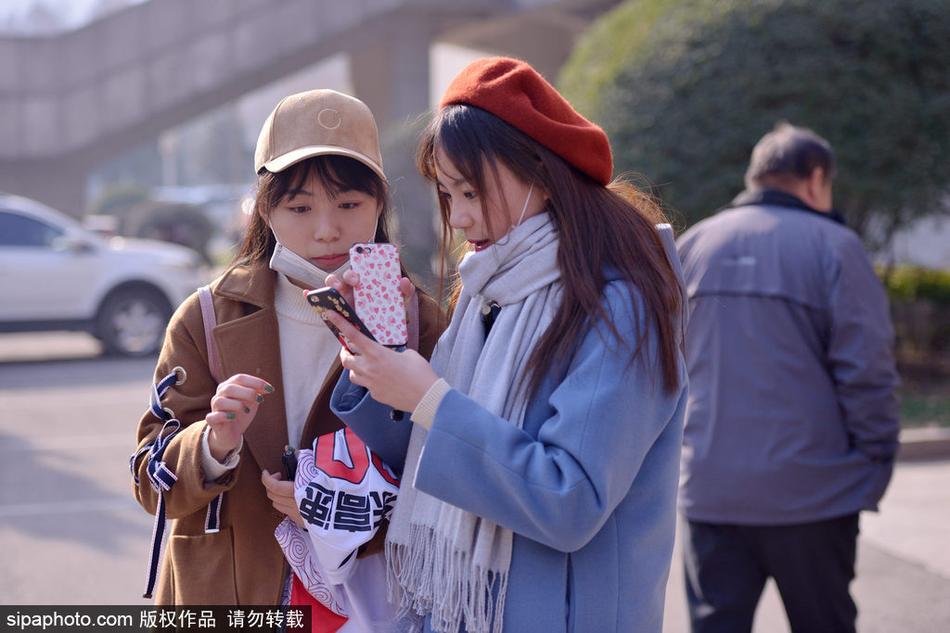 体育馆外的铁栏杆旁,几位年轻的女球迷聚在一起,有的低头摆弄手机,有的则翘首望向场馆内部,她们随身携带的背包上挂着球队的周边饰物。