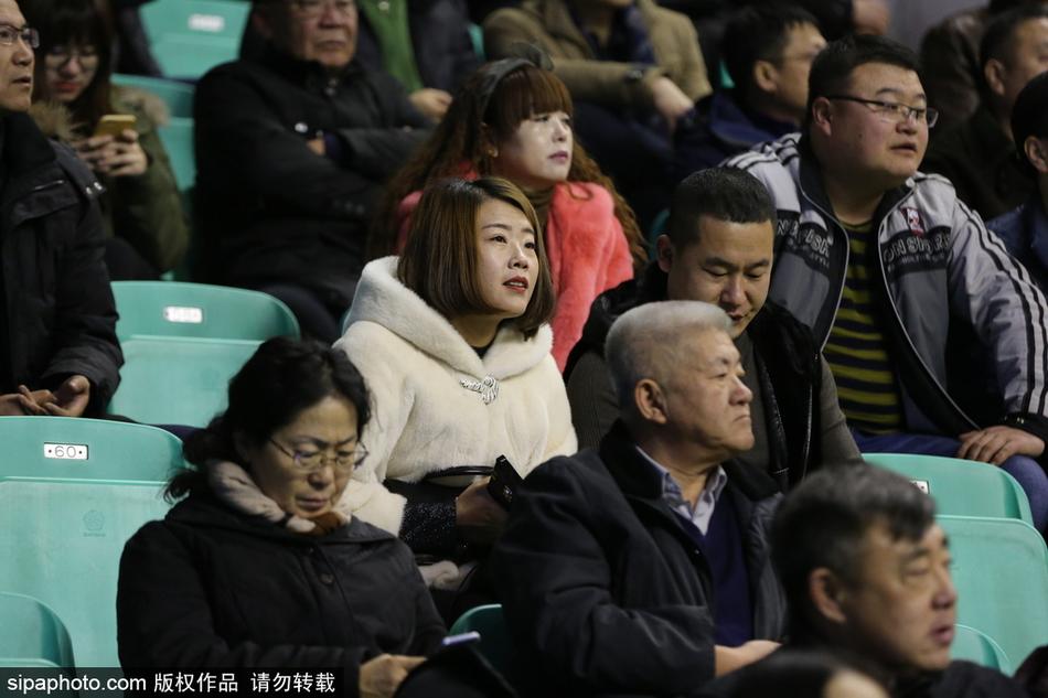 寒夜里，一位身着深色貂绒大衣的男球迷双手插兜，目光如炬地关注着场内局势，昂贵的衣装与他对篮球的专注神情相得益彰。