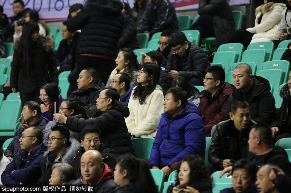 赛后，一位穿着白色貂绒大衣的女性球迷在场边自拍留念，背景是正在退场的球员和兴奋的观众，她想用这张照片记录下这个豪迈又温暖的胜利之夜。