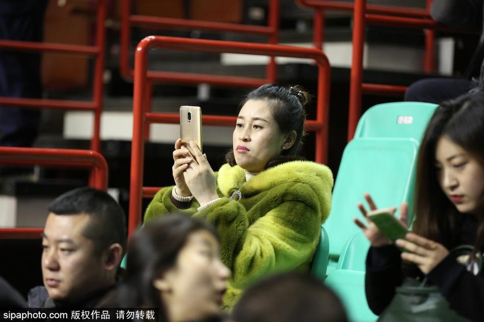 一位年轻球迷将貂绒大衣搭在肩上，内搭辽宁队的红色球衣，他面带笑容指着球场方向，仿佛在向同伴夸赞今晚主队的出色表现。