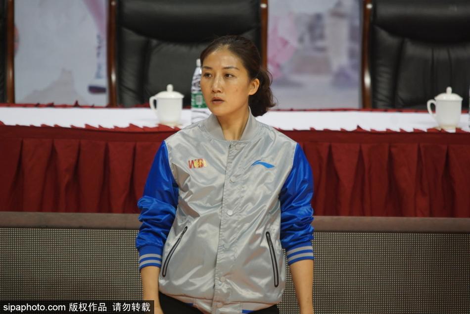 赛场中央,身穿深色裁判服的长发美女裁判目光如炬,她单手握拳,正准备吹响口中的哨子,严肃的神情与场边观众席上一位正在专注观看比赛的年轻女性形成了一种奇妙的静默呼应。