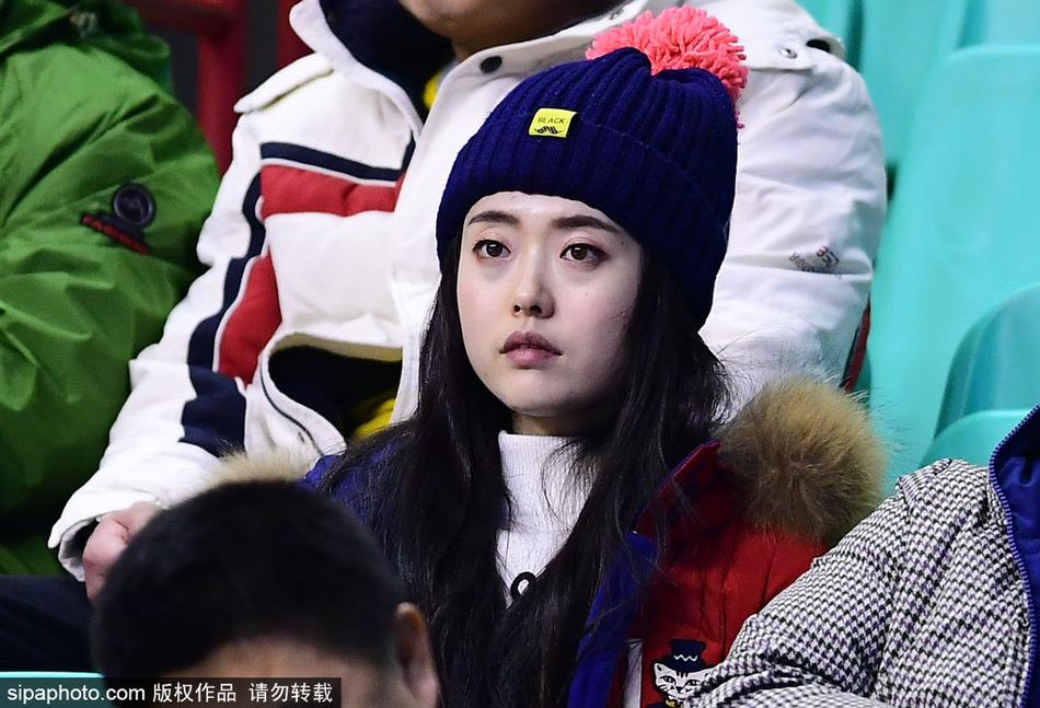 球场灯光的余晖洒在这位短发女孩的侧脸上，勾勒出一道迷人的金色轮廓。她微微侧身，眼神专注而深邃，仿佛能洞察球场上瞬息万变的战局，清冷的气质与身后热烈的氛围形成极具张力的对比。