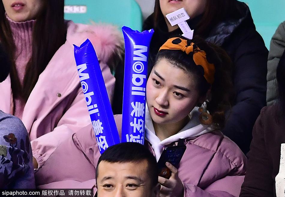 一名身穿深色V领上衣的女球迷正在低头查看手机,也许是在和朋友分享此刻激动的心情,又或是查看本场比赛的技术统计。即使是低头的瞬间,她精致的侧脸和柔顺的长发依然构成了一幅美好的画面。