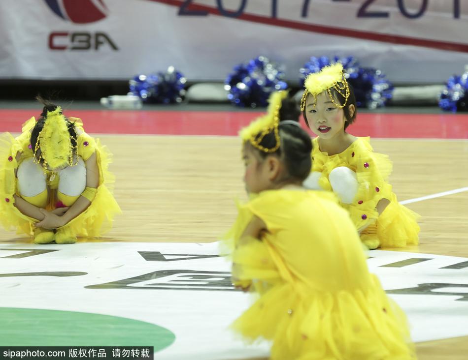 两名萌娃面对面站立,她们穿着统一的红色表演服,像是在相互鼓励或交流动作,稚拙的身高差和懵懂的表情让这一刻显得格外温馨可爱。