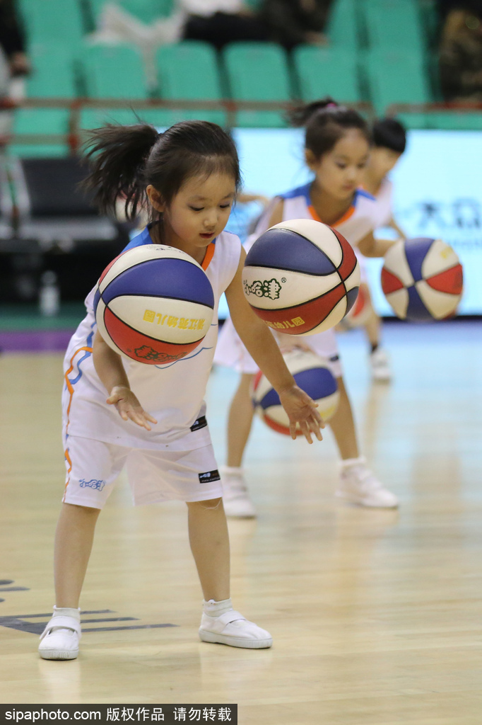 一个小女孩在表演中不慎滑倒,但她迅速爬起来,顾不上拍身上的灰尘,立刻找回节奏继续拍球,脸上依旧挂着甜甜的笑容,萌态可掬又惹人疼爱。