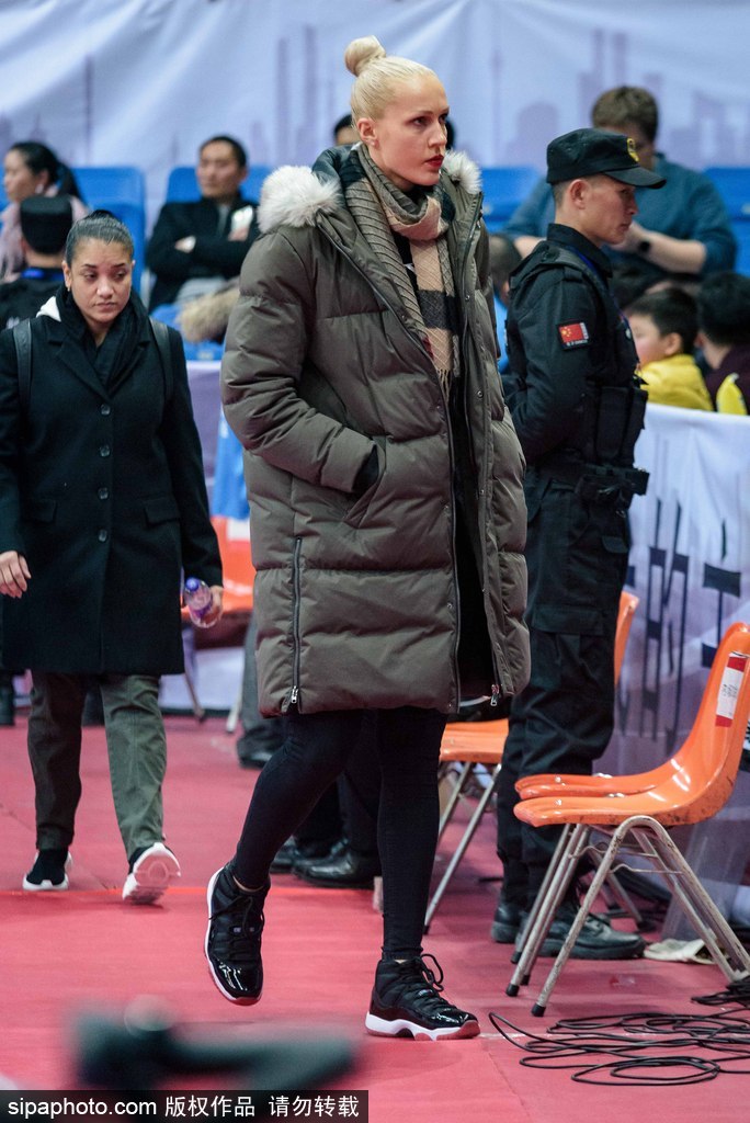 比赛间隙，这位四川女篮的外援神情放松地与同伴交流，她身着便装坐在看台上，仿佛一位普通的资深球迷，享受着现场热烈的篮球氛围。