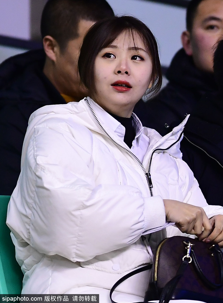 一位面容清秀的美女球迷身穿白色绒衣，双手举着助威加油牌，眼神专注地望着赛场方向，仿佛下一秒就要为心爱的球星呐喊出声。