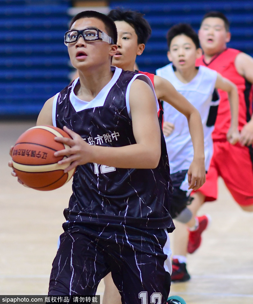 一名身穿蓝色球衣的小球员在三人包夹下依然高高跃起,眼神坚毅地完成投篮,他紧绷的肌肉和舒展的动作定格在空中,展现了篮球少年的蓬勃朝气。