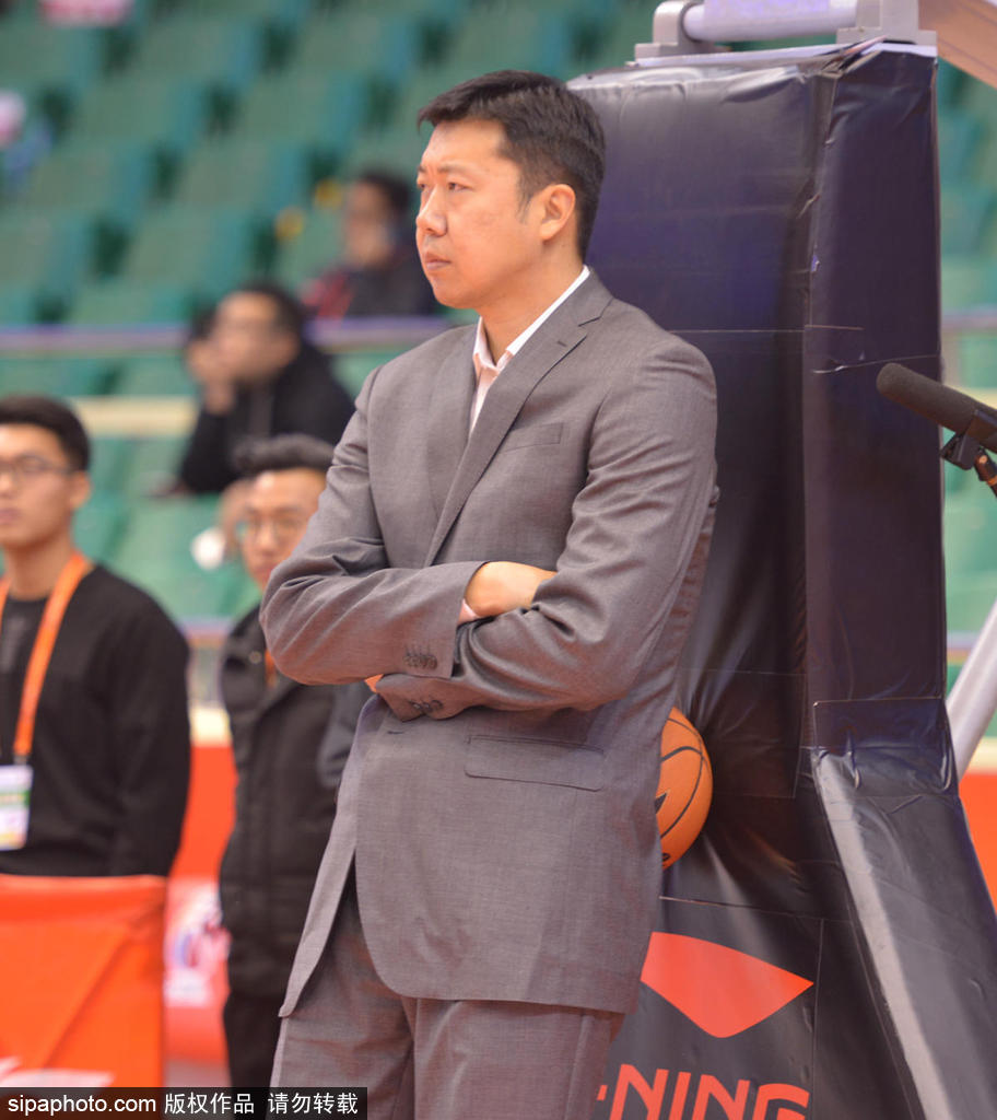 场边的王治郅眉头微蹙，双手依旧插在口袋里，他正在观察场地另一端的训练情况，背景是看台上星星点点的观众。