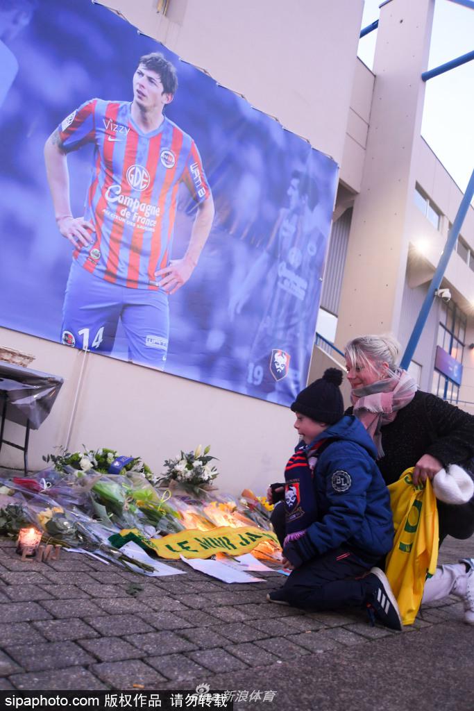 特写镜头下，球迷手中捧着的一束淡黄色鲜花，花束中插着一张萨拉进球后振臂欢呼的珍贵照片，花瓣上沾着点点雨滴，映衬着夜晚的灯光。