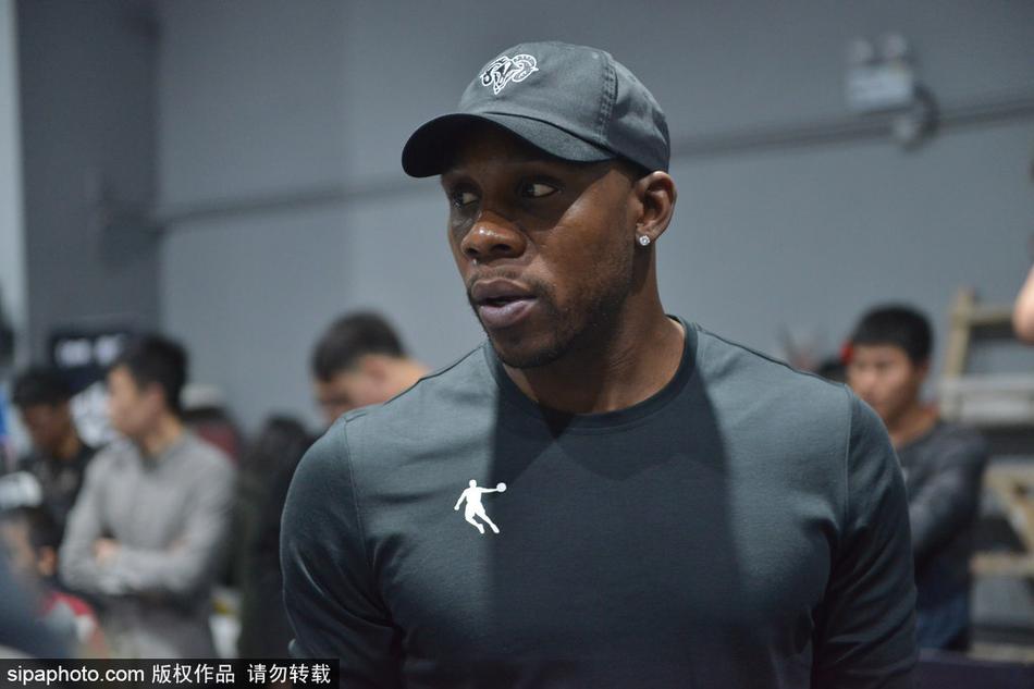 哈德森面带微笑，弯下腰耐心指导一位女球迷运球，眼神专注，场边围满了翘首以盼的观众。