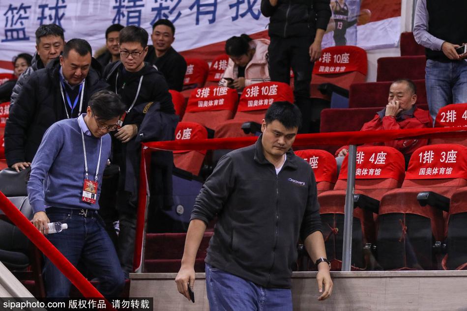 中国篮协主席姚明表情严肃地坐在北京奥体中心看台上，目光如炬地注视着场内激烈的比赛，他身着深色正装，在人群中显得格外高大醒目。