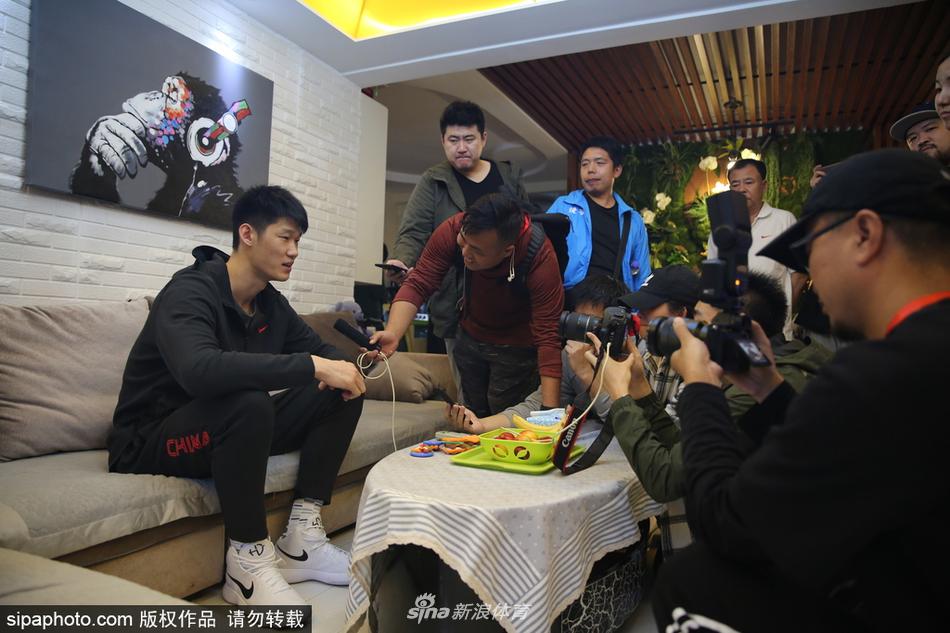 胡金秋将签名笔递还给球迷家的孩子，画面聚焦在他修长的手指和认真签下的名字上，背景是孩子父亲拿着手机记录这一珍贵时刻的模糊身影。