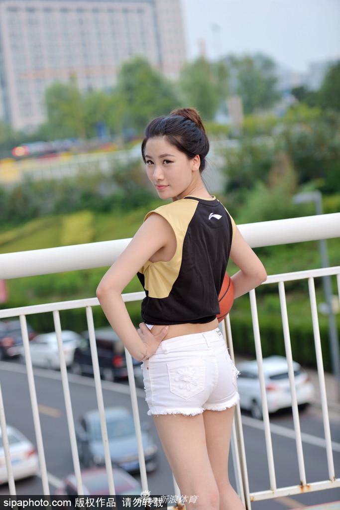 女球迷靠着围栏，身后是空旷的球场，悠然自得的神态宛如夏日精灵，浅色着装与蓝天白云完美融合。