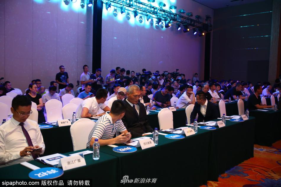 台上主持人正在宣读选秀结果，背后的大屏幕闪烁着各队LOGO，姚明在台下双手交叉于身前，神情严肃地注视着这一切，仿佛在守护着选秀大会的神圣。