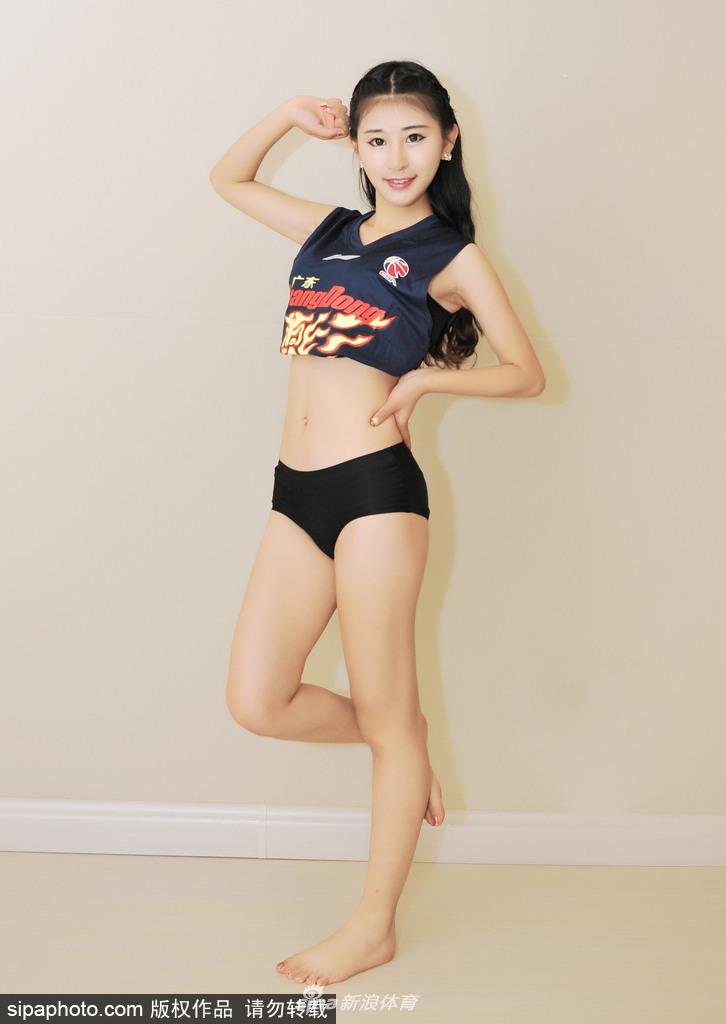 一位篮球宝贝坐在场边的篮球上，双手撑着膝盖，对着镜头露出灿烂的笑容，汗水仿佛还挂在额头，洋溢着青春的朝气。