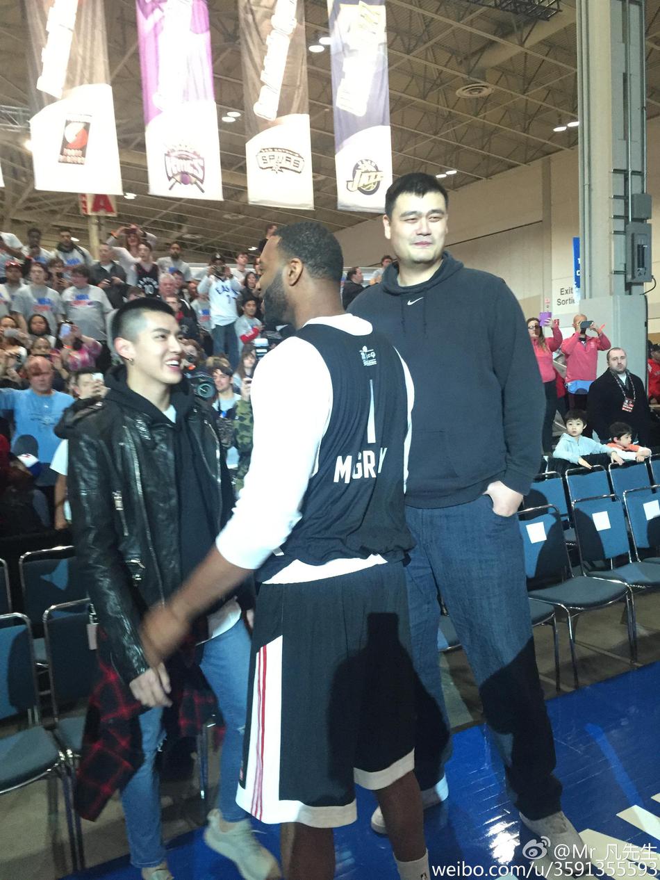 麦蒂身穿深色西装，面对镜头露出标志性的慵懒笑容，旁边的吴亦凡正专注地望向两位篮球传奇。