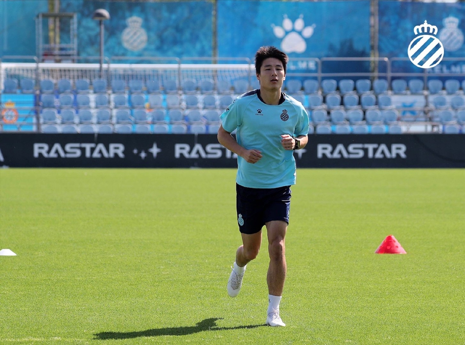 武磊在阳光下舒展步伐，身披西班牙人战袍慢跑，眼神坚定充满重生后的喜悦，仿佛在向世界宣告王者归来。