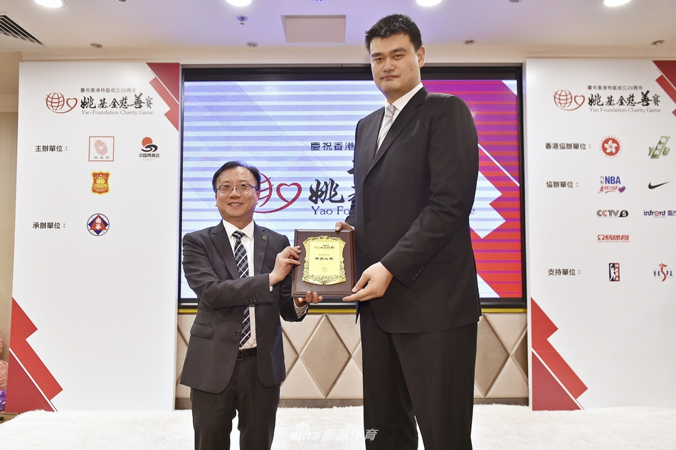 记者招待会现场，姚明正与身旁的一位男士低声交谈，两人神情专注而愉悦，展现了这位篮协主席在严肃公务之外的亲和力与交流热忱。