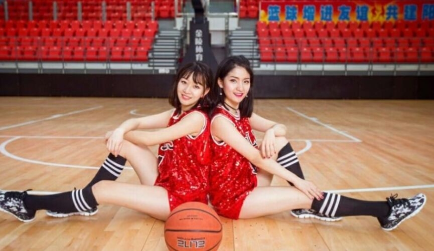 两位空姐篮球宝贝在赛前热身时默契击掌，一人身穿红色运动背心，一人身穿白色，健康的小麦色肌肤在阳光下闪着光。