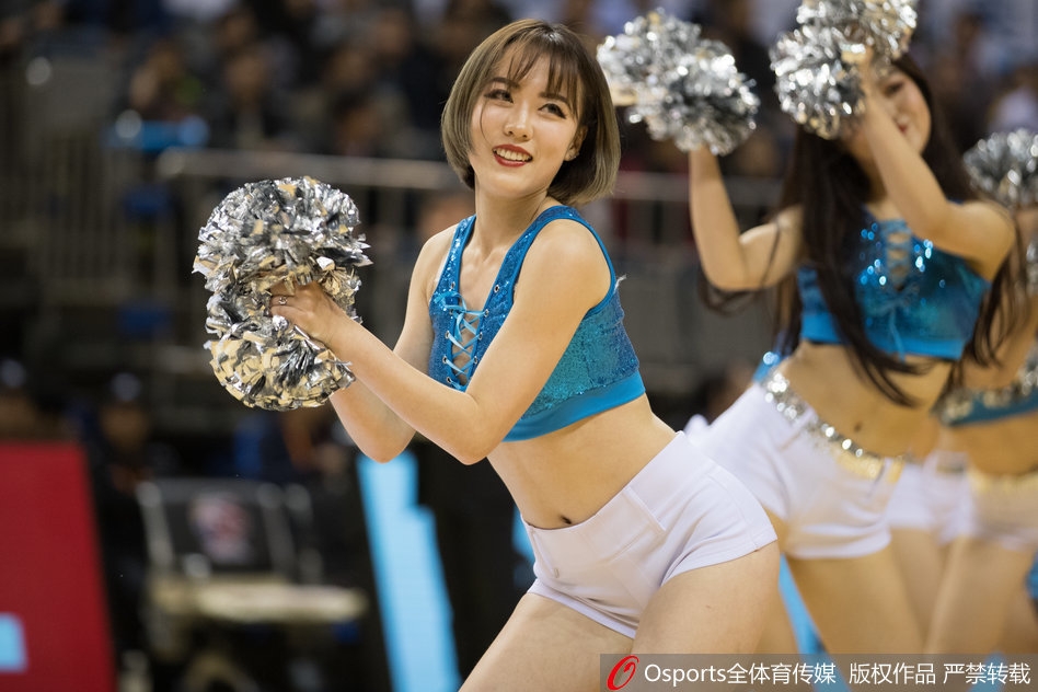 全景视角下，一群篮球宝贝侧身排开，高举双手舞动，现场地板反射着灯光，营造出热烈的赛场氛围