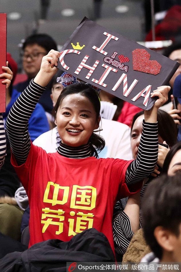 赛场边的看台上,一位身穿应援服的女生回眸一笑,手中紧握着助威旗帜,身后是沸腾的人群,她的眼神明亮而坚定,仿佛在说:这一刻,我与球队同在。