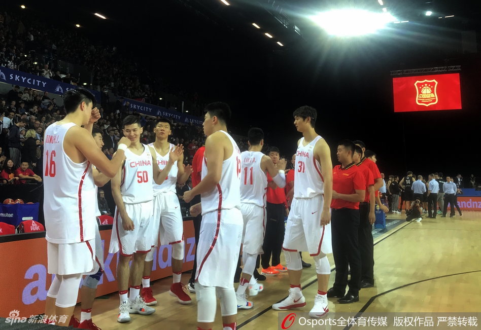 中国队球员在三分线外果断出手，篮球在空中划出优美的弧线，背景是新西兰队员奋力扑防的瞬间，展现了男篮球员敢于担当的决心。