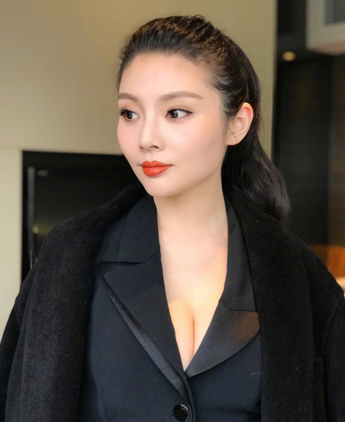 徐冬冬身着一袭剪裁利落的黑色皮裙，坐在地毯上回眸凝视，杏眼迷离，红唇如花瓣般娇艳，修长双腿在黑裙映衬下更显白皙，整个人散发出复古女郎的慵懒与魅惑。