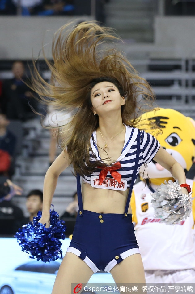 侧面特写捕捉到一名长发宝贝旋转的瞬间，虎尾造型的腰饰随着身姿摆动，脸上洋溢着自信的微笑，背景是虚化的球迷看台，整个画面充满动感与张力