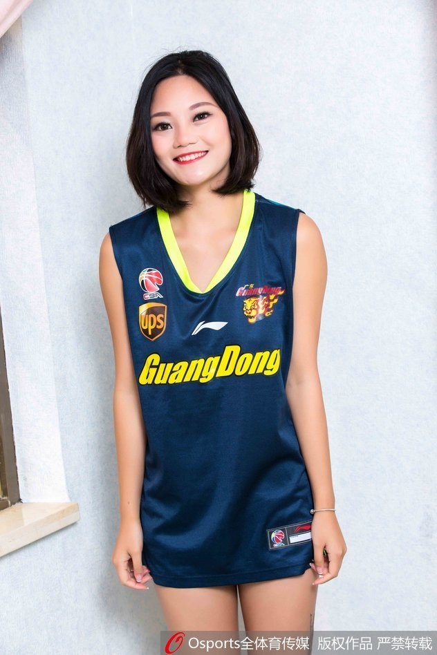 女孩蹲坐在场边的广告牌旁，单手托腮，宽松的球衣下露出灿烂的笑容，甜美可爱的气质成为赛场边的一抹亮色。