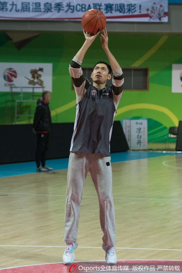 体能教练受到丁彦雨航的感染,正聚精会神地从篮架后方尝试高难度投篮,队友们站在一旁准备抢篮板,脸上洋溢着轻松的笑容。