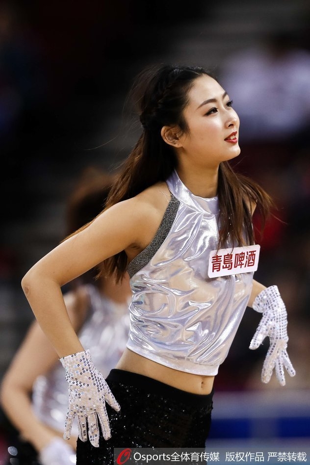 特写镜头中，一位篮球宝贝俯身摆出酷炫的定格姿势，金色的短上衣在灯光下熠熠生辉，深邃的眼妆和自信的嘴角，透露出职业啦啦队员的专业素养与独特魅力