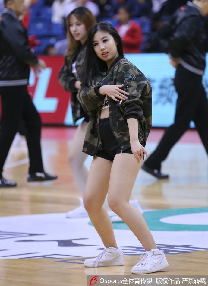 一位青岛啦啦队员在表演间隙独自站在场边，她扎着高马尾，若有所思地看向远方，身后的看台上坐满了热情的观众。这张照片展现了篮球宝贝在喧闹赛场中难得一见的安静与柔美。
