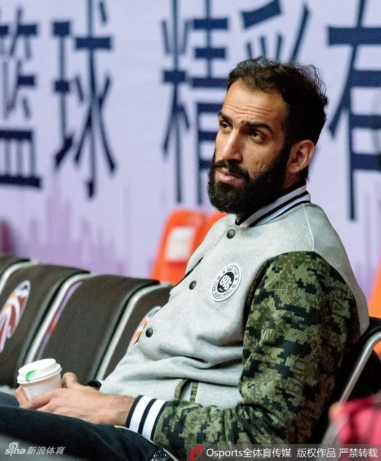 哈达迪与队友在场边交流,他紧握冒着热气的杯子,身旁的年轻球员认真聆听这位老大哥的指点。