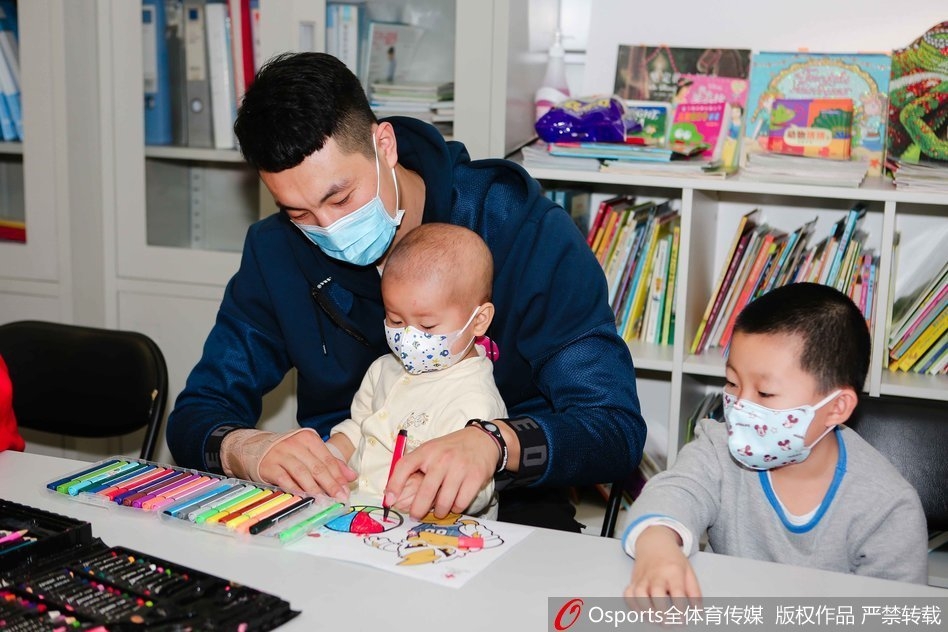 翟晓川盘腿坐在地板上,与几个戴着口罩的小朋友围成一圈,他正拿着一个彩色气球逗其中一个孩子,孩子们咯咯笑着伸手去够,场面温馨如同一个大哥哥带着弟弟妹妹做游戏