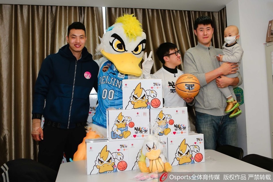 身穿红色队服的翟晓川和张松涛半蹲在病床前,手里拿着彩色画笔,正温柔地与戴着口罩的小朋友一起涂鸦,病床上的小桌板成了临时的画桌,孩子的眼神专注而明亮