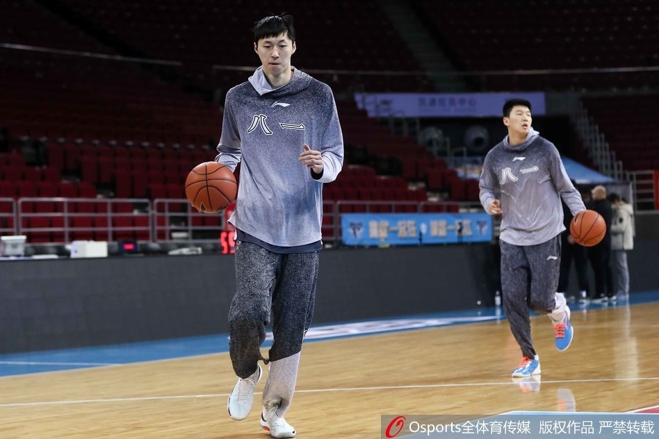 王治郅双手持球置于身前,正面指导一位八一队员,两人目光交汇,正在进行着关于战术跑位的深度交流,空气中弥漫着专注与严肃的气息。