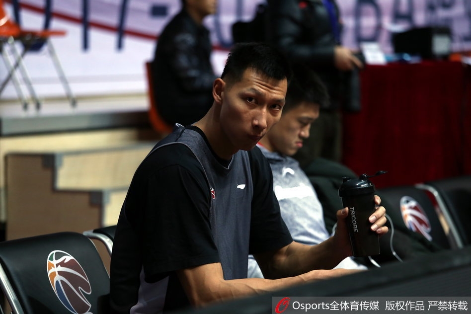 队友在一旁练习运球突破，易建联则站在篮下稍作调整，他拿起放在地上的大号水壶，仰头畅饮，喉结上下滚动，汗水沿着脸颊滑落。