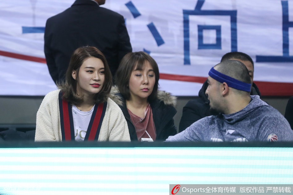 李根妻子与西热力江在场边低声交谈,两人神情专注,西热力江比划着手势,似乎正在分享着关于场上局势的什么秘密。