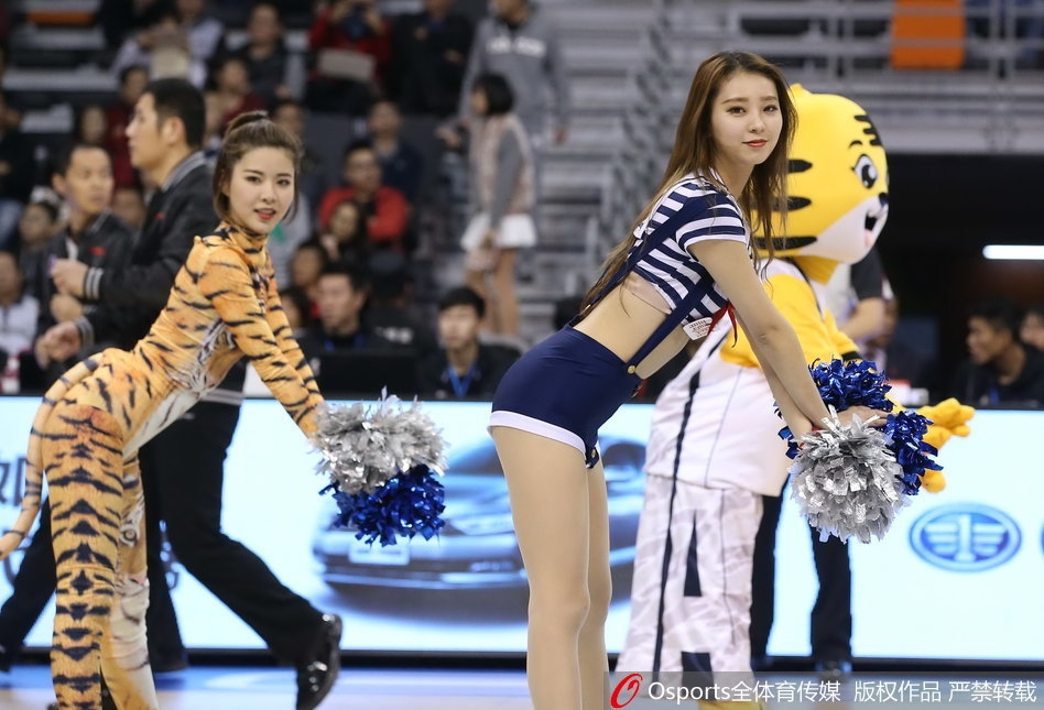 全景视角下，六位篮球宝贝摆出虎踞造型的结束 pose，她们错落有致地分布在球场中央，橙色的服装在深蓝色的地板上格外醒目，宛如盛开在赛场上的烈焰之花