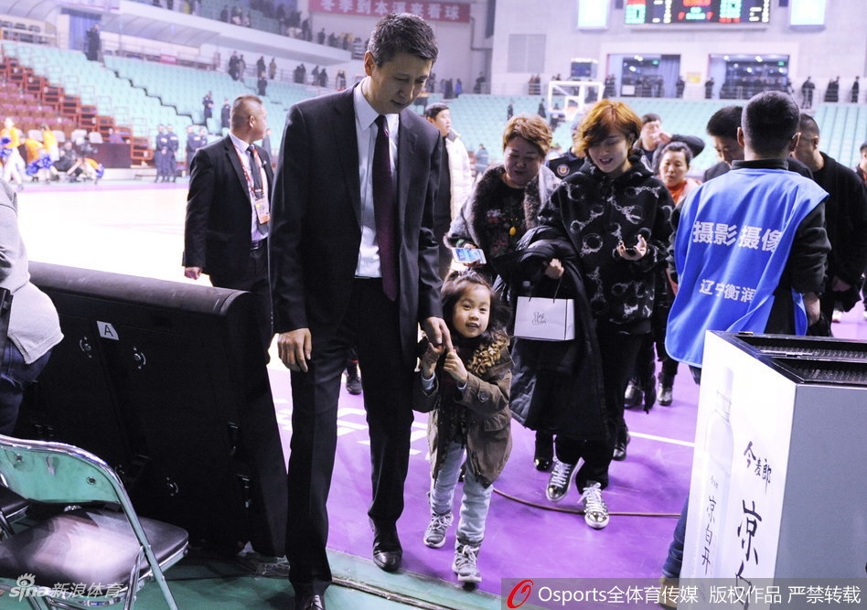 赛场灯光下，辽宁队主帅郭士强西装笔挺，怀中抱着可爱的女儿准备退场，小公主扎着俏皮的小辫子，好奇地望着四周还未散去的观众，父女俩构成一幅温馨的画面