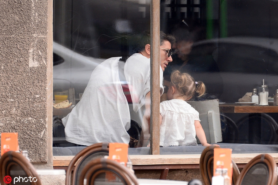 莱万目光温柔地注视着小女儿，小女孩在马路上张开双臂，仿佛一只想要飞翔的小鸟，父女间的互动充满了童趣。