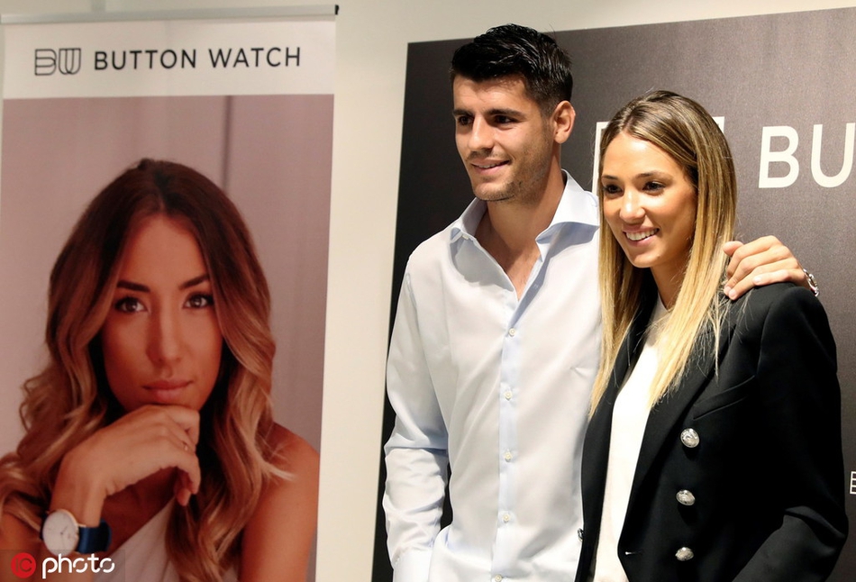 活动现场的莫拉塔专注地调试腕表，眼神中透露出一丝不苟的专注，身边的爱丽丝则侧身关注着丈夫，细节处尽显默契