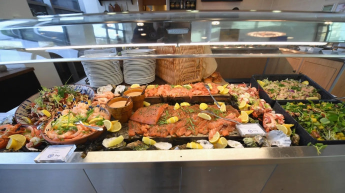 队长阿斯皮利奎塔站在临时搭建的小舞台上，手持麦克风，似乎正在进行一段即兴的圣诞祝词，队友们在台下鼓掌起哄，气氛热烈。