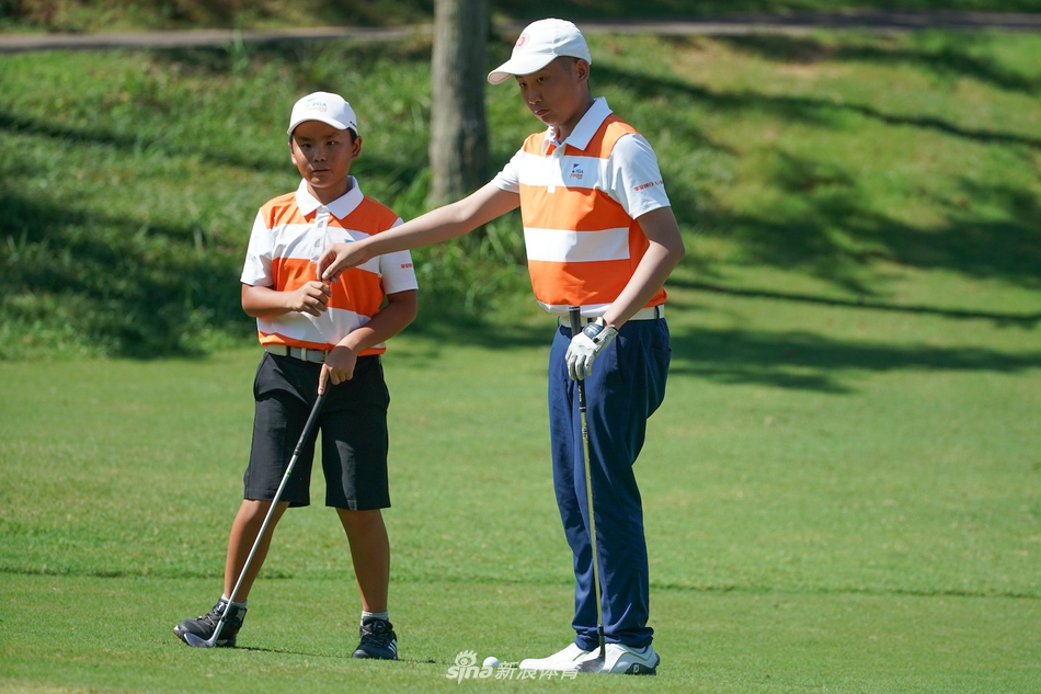 两位小搭档在果岭上并肩而立，共同低头审视推杆线路，阳光将他们的身影拉长，画面充满默契与专注。